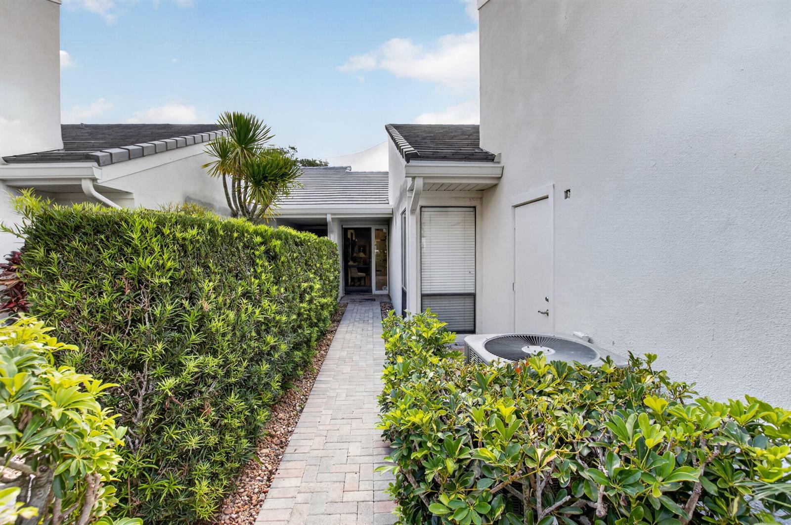 A brick walkway leads to a front entrance between two white buildings with hedges — 19950 Sawgrass Lane # 5203, Boca Raton FL 33434, BOCA RATON, FL