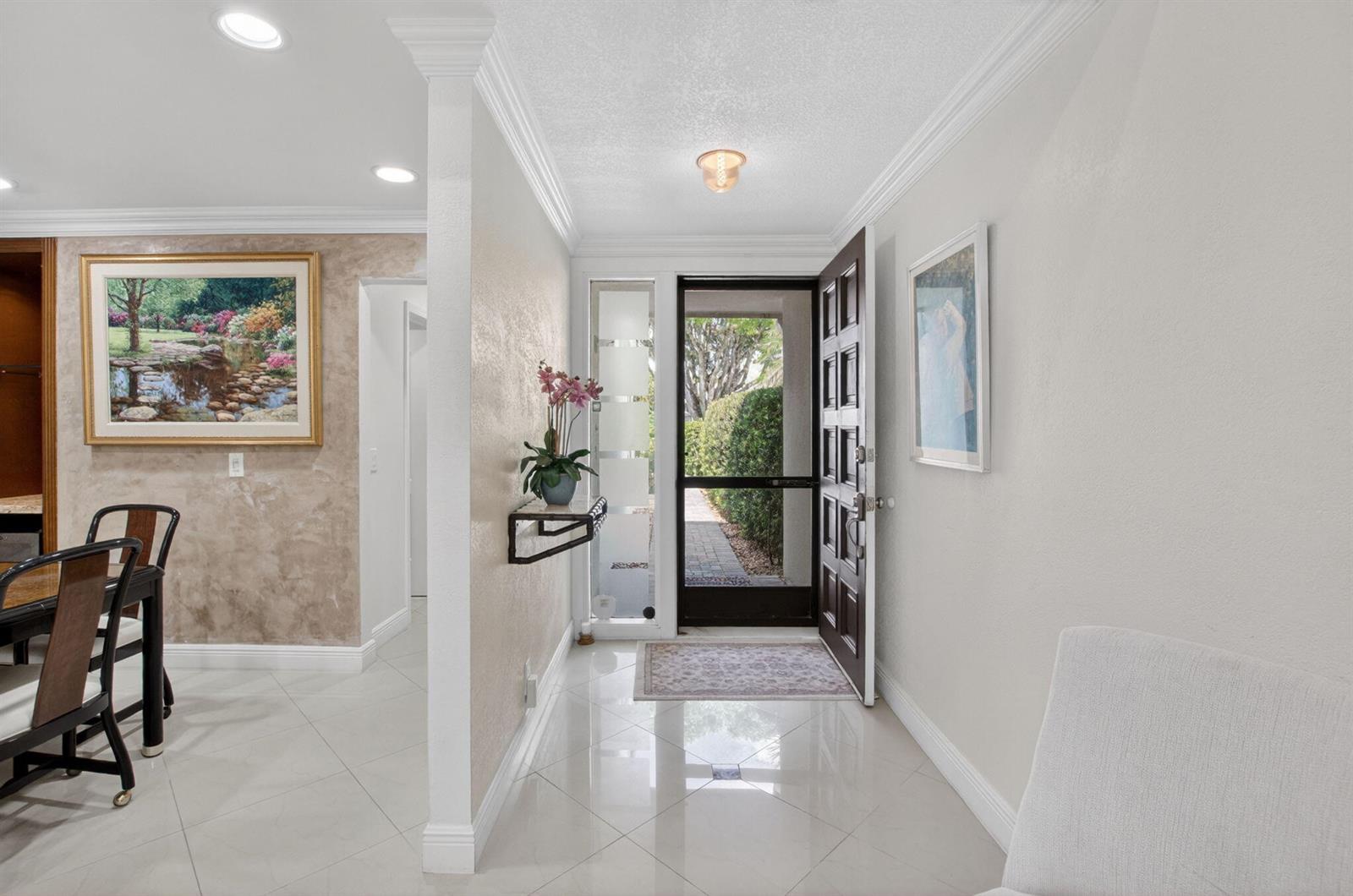 A bright entryway features a dark wood front door, tiled floors, and a wall-mounted shelf — 19950 Sawgrass Lane # 5203, Boca Raton FL 33434, BOCA RATON, FL