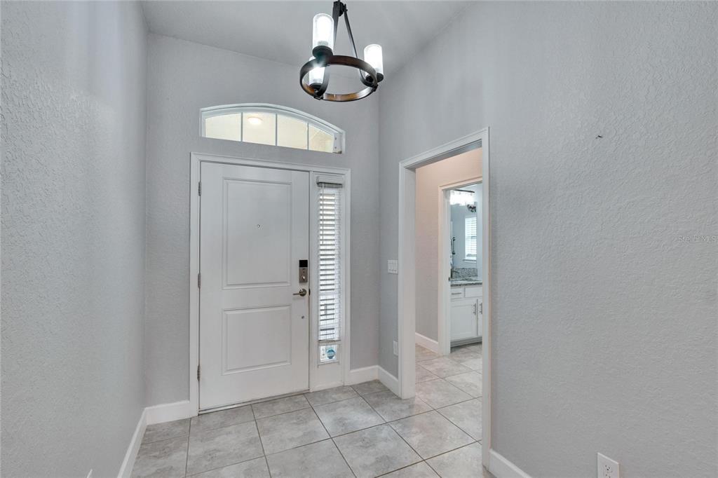 A tiled entryway features a white front door, a transom window, and a modern chandelier — 14525 SCOTTBURGH GLEN DRIVE, WIMAUMA, FL