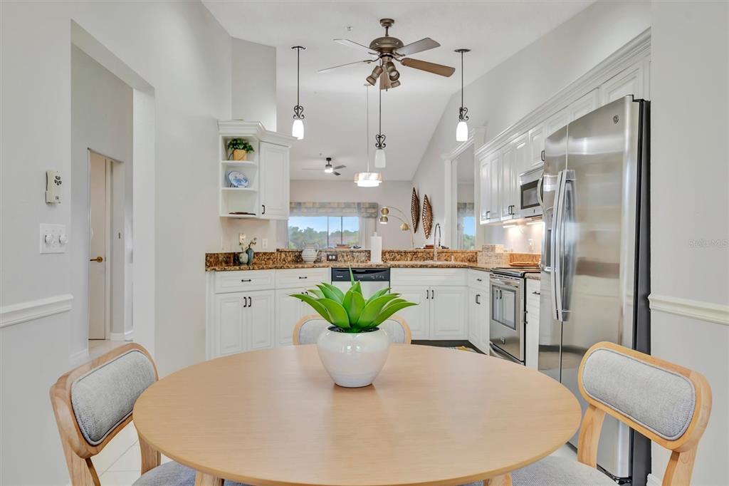 A kitchen with white cabinets, granite countertops, and a round wooden dining table — 5240 HYLAND HILLS AVENUE UNIT 1421, SARASOTA, FL