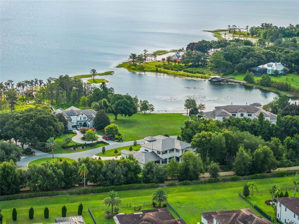 An aerial view shows several large houses situated on a grassy lot near a lake — 12624 PARK AVENUE, WINDERMERE, FL