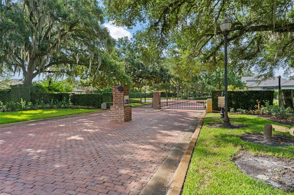 A brick-paved driveway leads to a gated entrance with brick pillars and mature oak trees — 12624 PARK AVENUE, WINDERMERE, FL