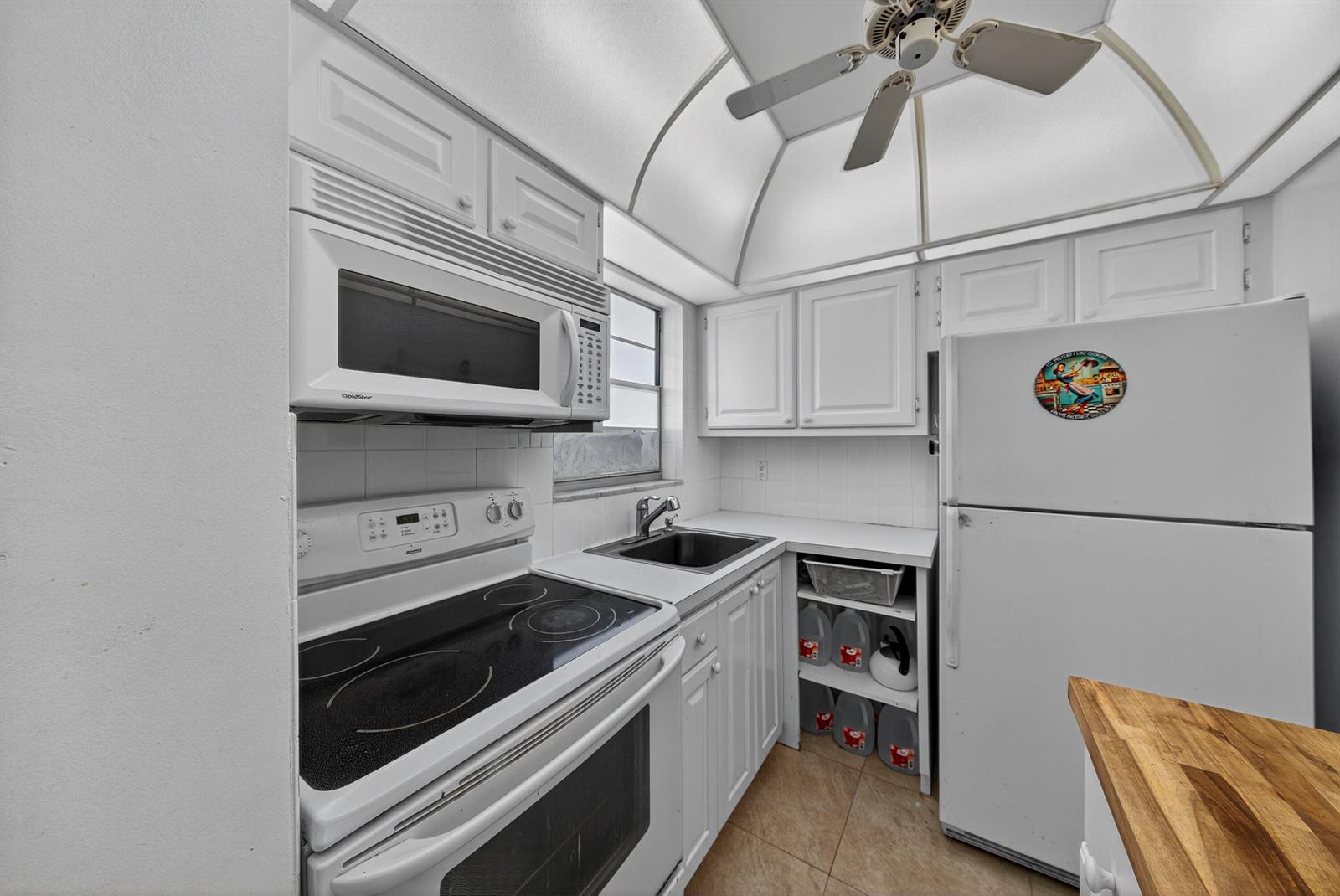 A white kitchen features a stove, microwave, sink, and a view into an adjacent room — 251 S GOLF Boulevard # 287, Pompano Beach FL 33064, POMPANO BEACH, FL