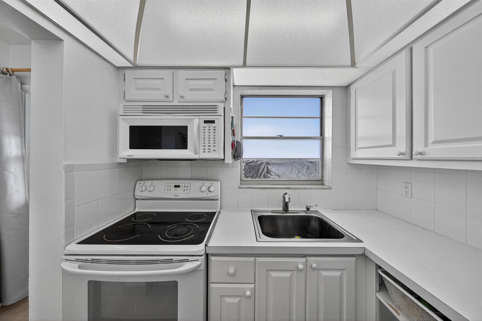 A white kitchen features a glass-top stove, microwave, refrigerator, and a vaulted ceiling with fan — 251 S GOLF Boulevard # 287, Pompano Beach FL 33064, POMPANO BEACH, FL