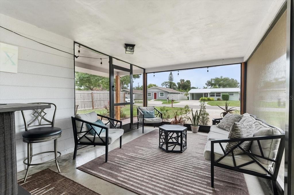 A screened-in porch features a concrete floor, outdoor furniture, and views of a residential street — 980 CHARLOTTE AVENUE, SARASOTA, FL