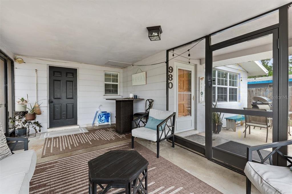 A covered patio features a black door, a screen enclosure, and outdoor furniture on rugs — 980 CHARLOTTE AVENUE, SARASOTA, FL
