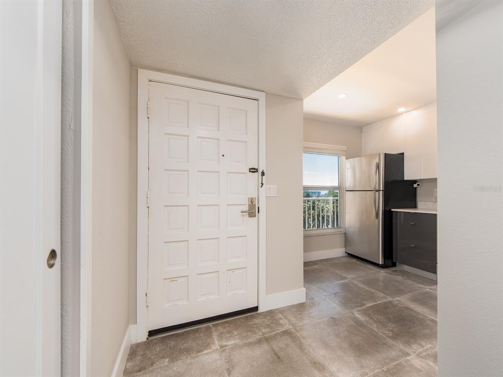 An entryway with a white door and tiled floor leads into a kitchen with stainless appliances — 105 ISLAND WAY UNIT 143, CLEARWATER, FL