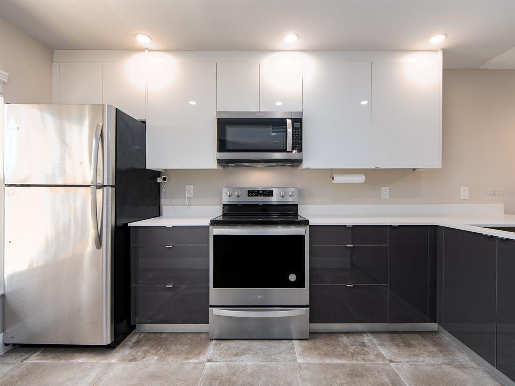 A kitchen features white upper cabinets, dark gray lower cabinets, and stainless steel appliances — 105 ISLAND WAY UNIT 143, CLEARWATER, FL
