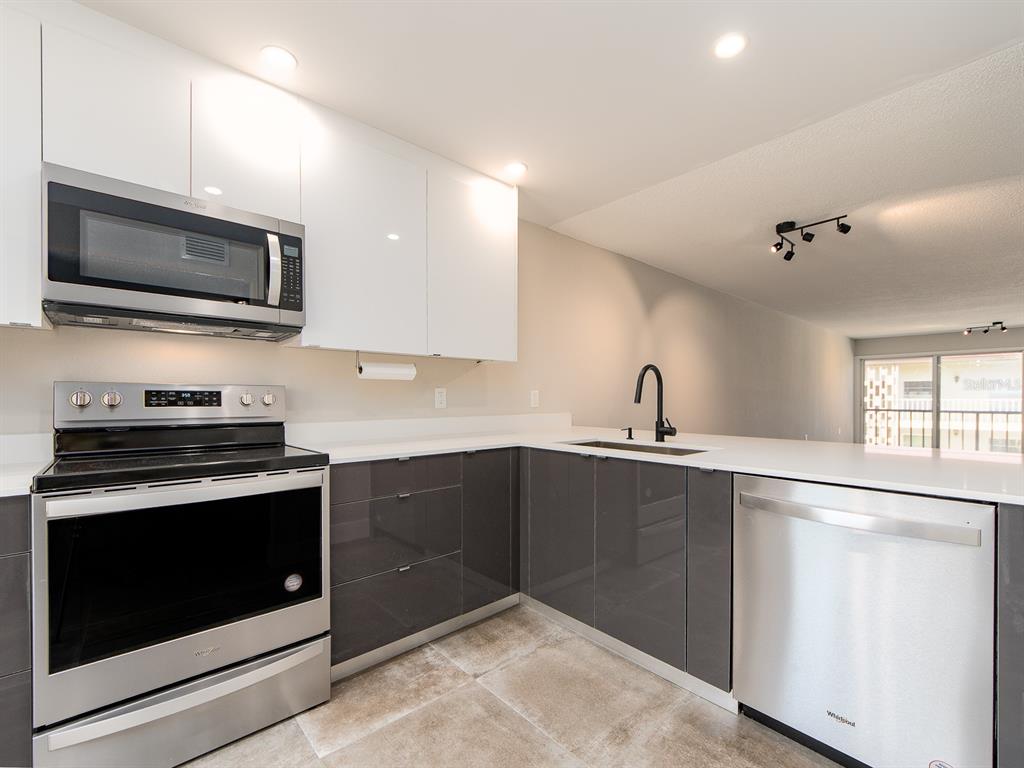 A modern kitchen features white upper cabinets, gray lower cabinets, stainless steel appliances, and tile flooring — 105 ISLAND WAY UNIT 143, CLEARWATER, FL
