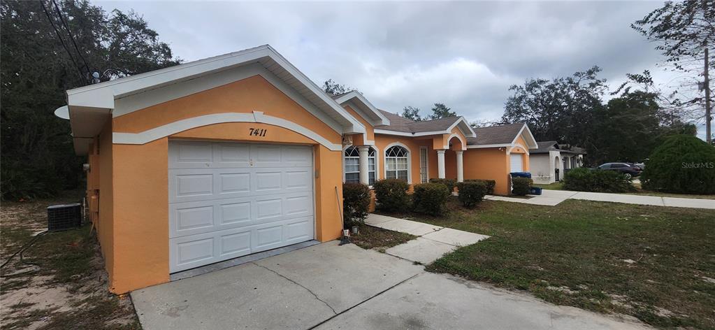 A single-story orange house with a white garage door and a concrete driveway — 7411 CANTERBURY STREET, SPRING HILL, FL