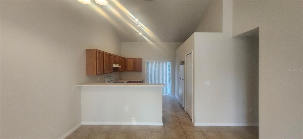 A kitchen with wood cabinets and a breakfast bar overlooks a room with tile flooring — 7411 CANTERBURY STREET, SPRING HILL, FL