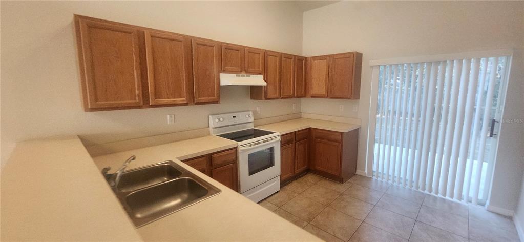 A kitchen features oak cabinets, white appliances, laminate countertops, and a sliding glass door — 7411 CANTERBURY STREET, SPRING HILL, FL