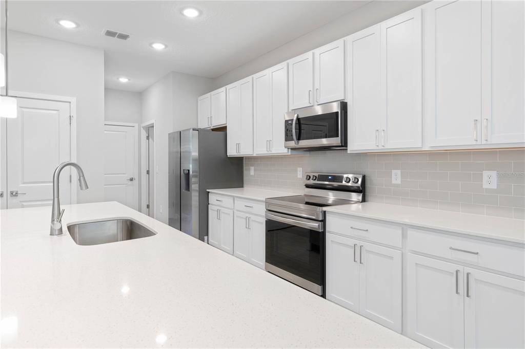 A modern kitchen features white cabinets, stainless steel appliances, and a large quartz island — 13 SW 34TH PLACE, CAPE CORAL, FL