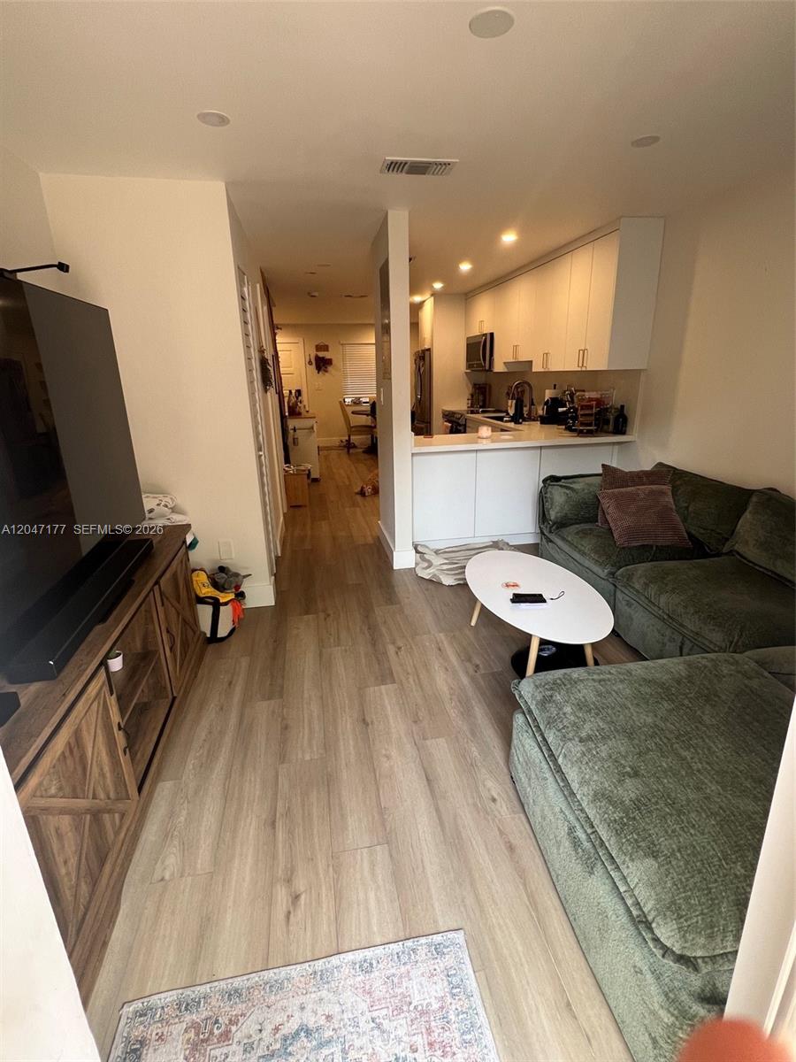 This living room features wood-look flooring, a green sectional sofa, and an open kitchen — 13338 SW 59th Ter, Miami FL 33183, MIAMI, FL