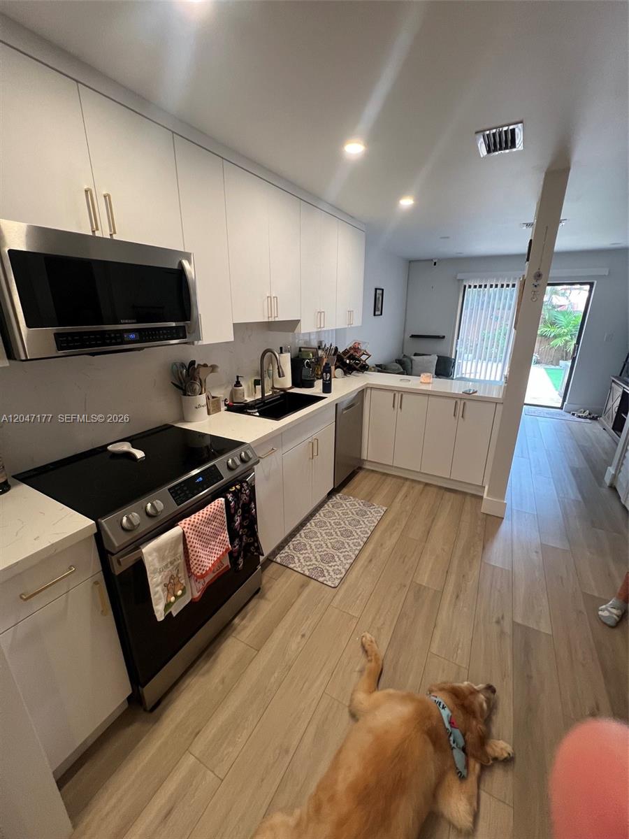 A kitchen with white cabinets, stainless steel appliances, and wood-look flooring features a resting dog — 13338 SW 59th Ter, Miami FL 33183, MIAMI, FL
