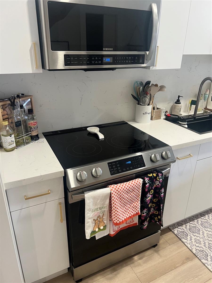 A modern kitchen features white cabinets, a stainless steel microwave, and a black electric range — 13338 SW 59th Ter, Miami FL 33183, MIAMI, FL