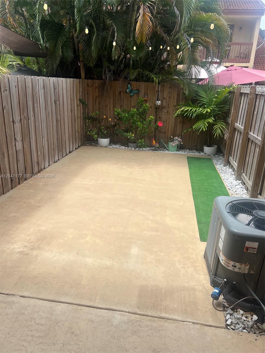 A fenced concrete patio features potted plants, string lights, and an outdoor air conditioning unit — 13338 SW 59th Ter, Miami FL 33183, MIAMI, FL
