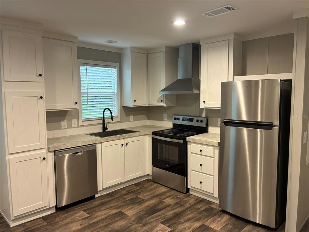 A kitchen features white cabinets, stainless steel appliances, a black sink, and wood-look flooring — 263 EDGEWOOD BOULEVARD, LAKE WALES, FL