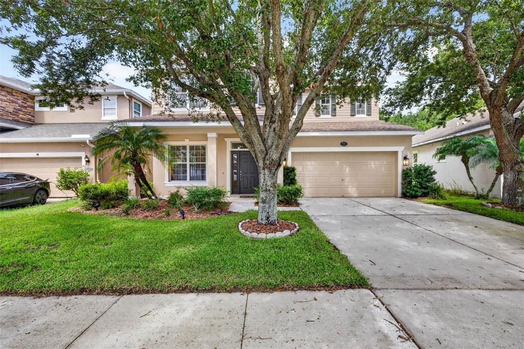 A two-story suburban house with a tan exterior, a two-car garage, and a front lawn — 7906 CAMDEN WOODS DRIVE, TAMPA, FL