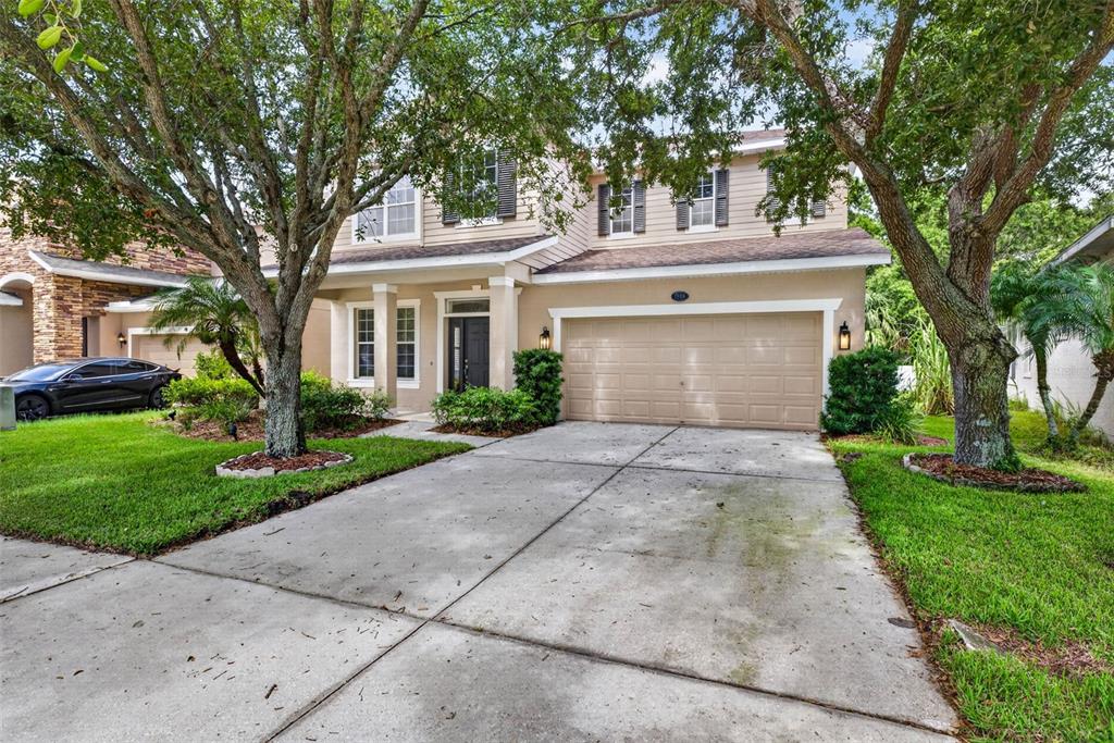 A two-story suburban house with a beige exterior, a two-car garage, and mature trees — 7906 CAMDEN WOODS DRIVE, TAMPA, FL