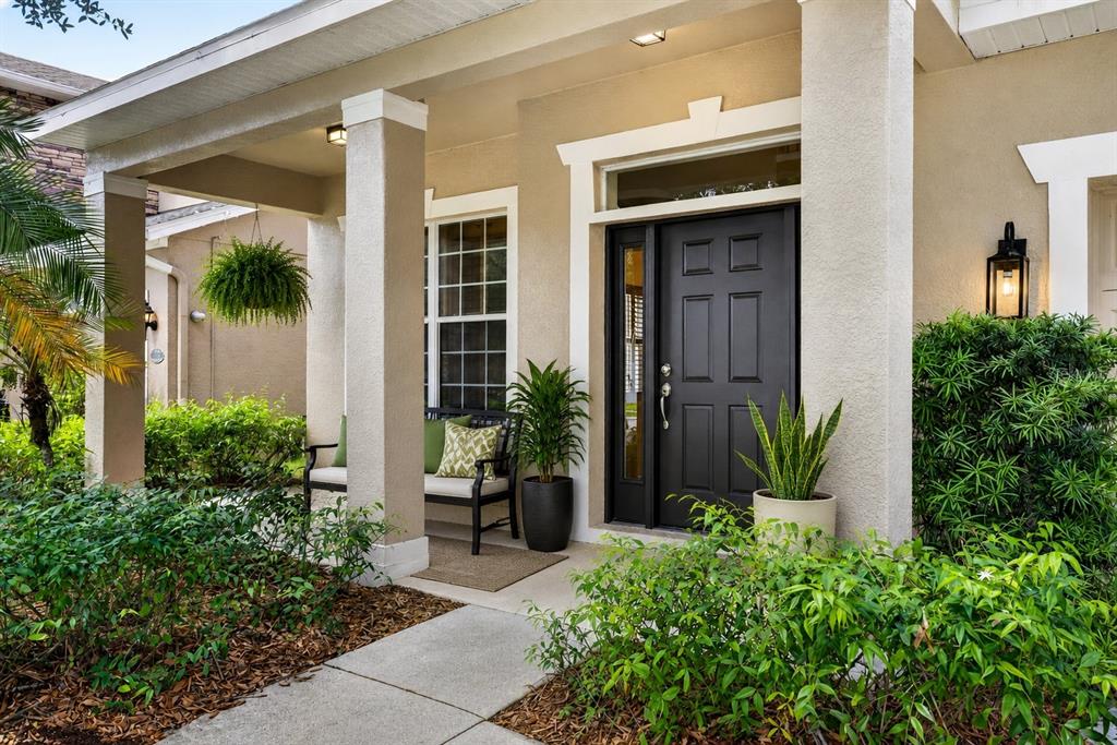 A front porch features a dark door, a bench, potted plants, and a concrete walkway — 7906 CAMDEN WOODS DRIVE, TAMPA, FL