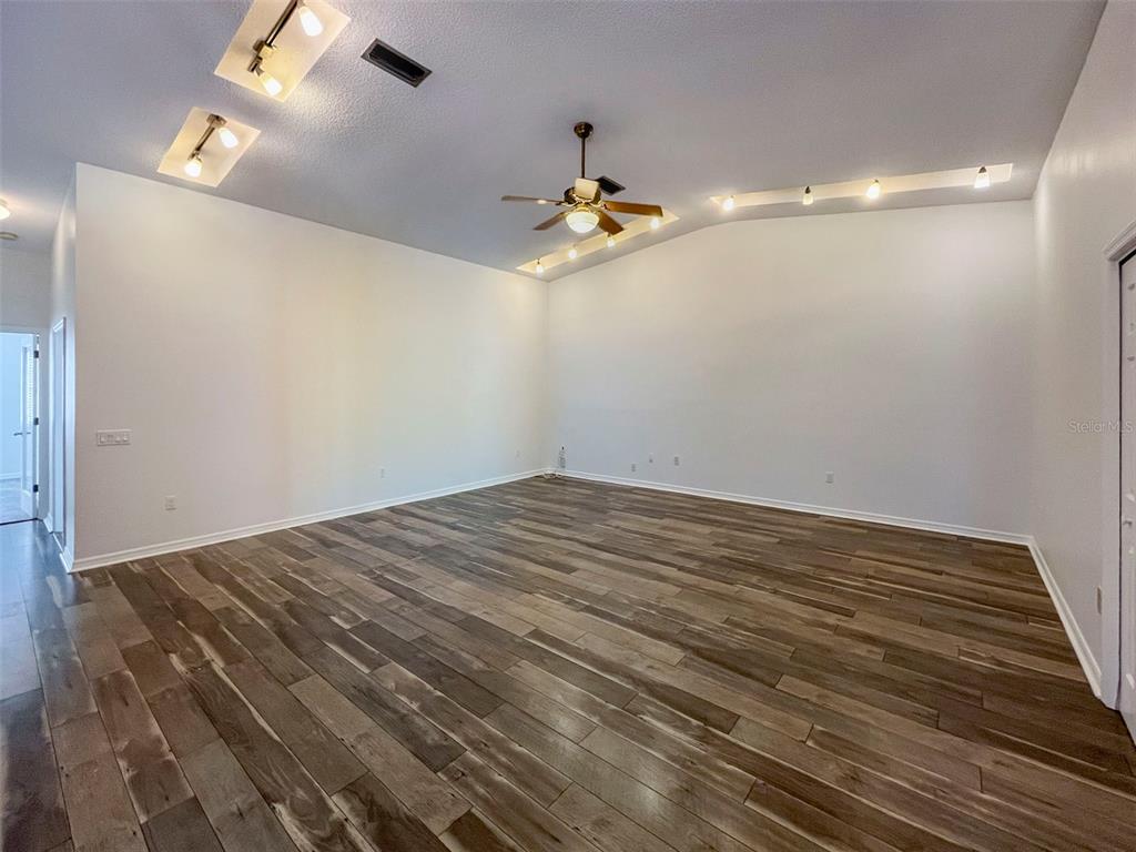 An empty living room features wood-look flooring, a ceiling fan, and recessed cove lighting — 3957 PROCTOR ROAD, SARASOTA, FL