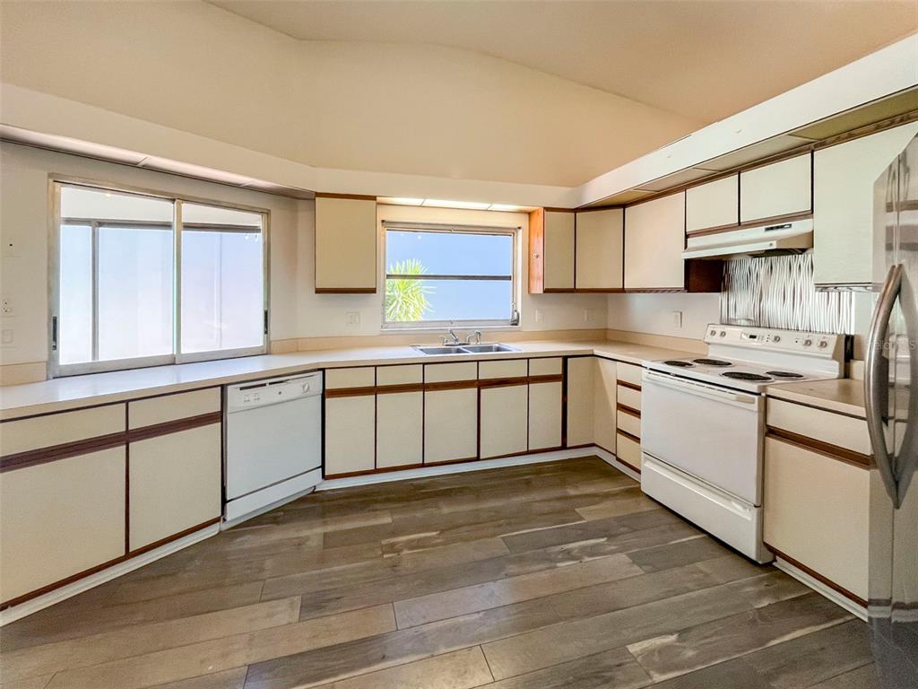 A kitchen features white cabinets with dark trim, white appliances, and wood-look flooring — 3957 PROCTOR ROAD, SARASOTA, FL