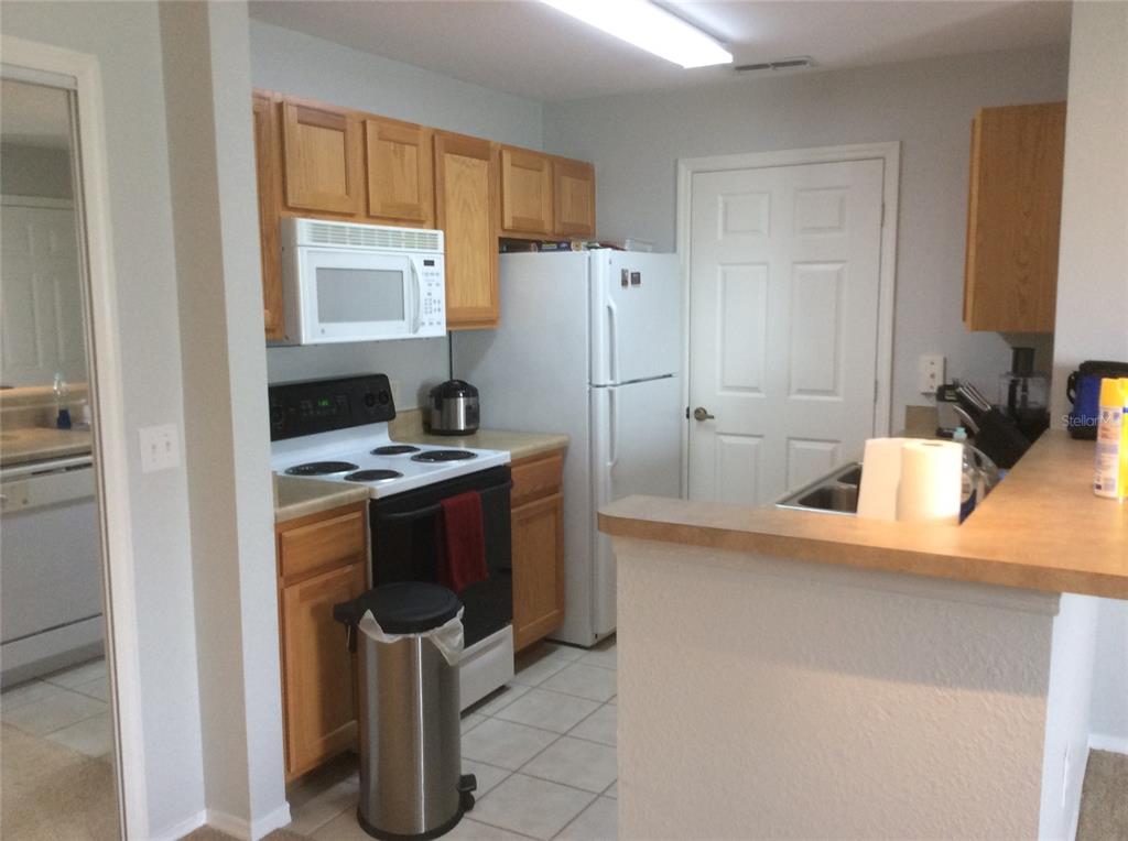 A kitchen features light wood cabinets, white appliances, tile flooring, and a breakfast bar — 4850 51ST STREET W UNIT 5107, BRADENTON, FL