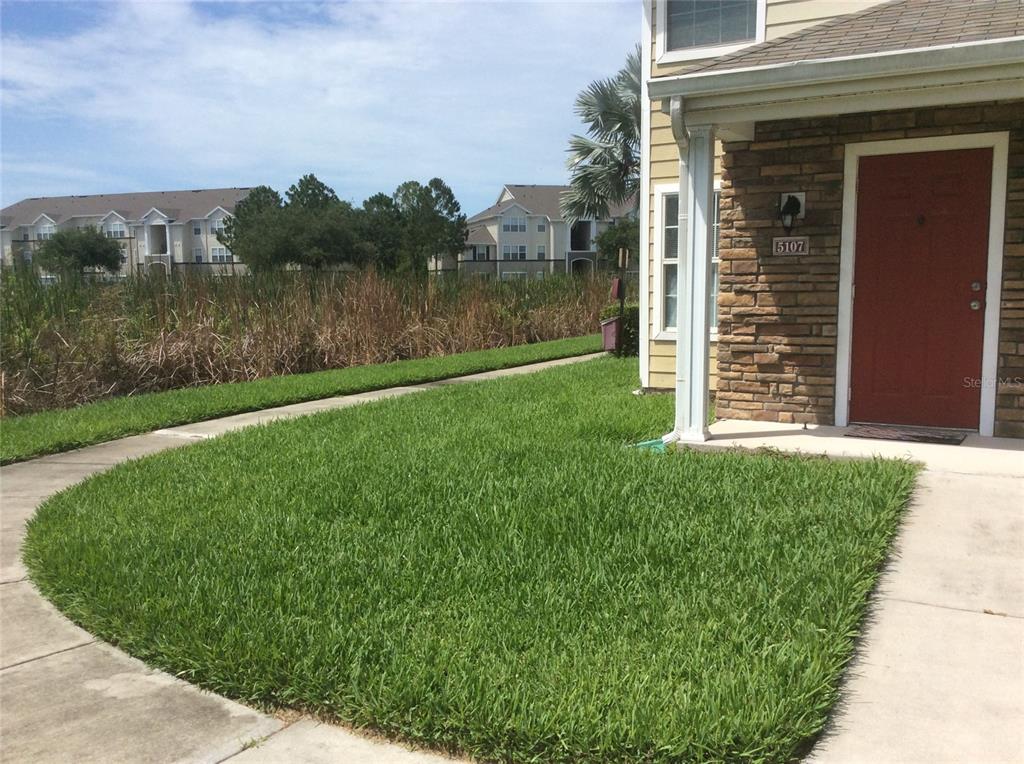 A view of a residential building exterior with a red front door and lawn — 4850 51ST STREET W UNIT 5107, BRADENTON, FL