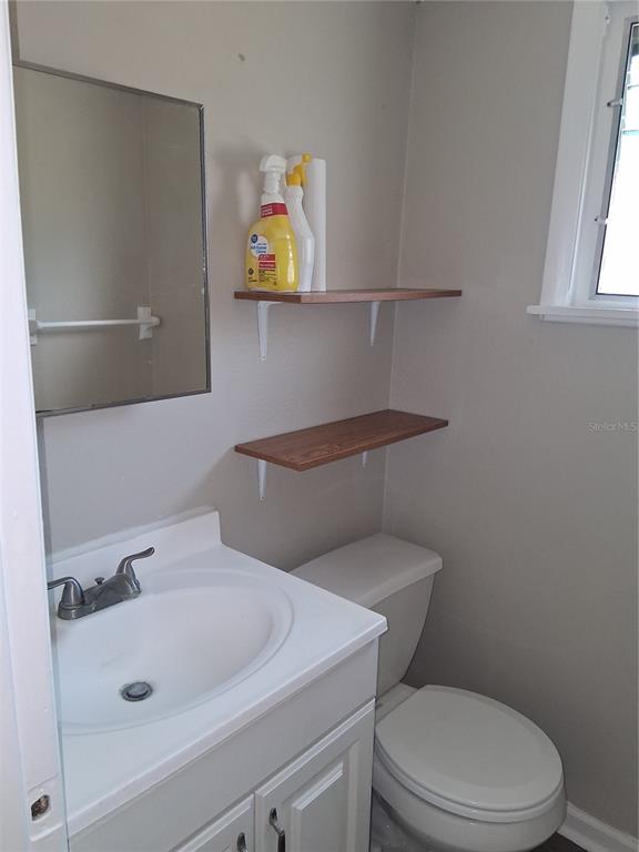A small bathroom features a white vanity, a mirror, two wooden shelves, and a toilet — 1123 15TH AVENUE NW UNIT N, LARGO, FL