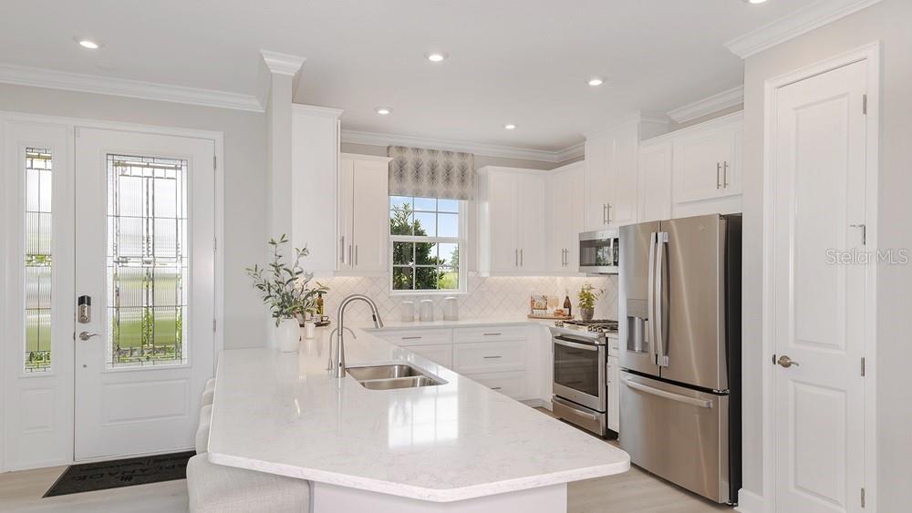 A bright kitchen features white cabinets, stainless steel appliances, and a large quartz-topped island — 7528 MOONBEAM AVENUE, SARASOTA, FL