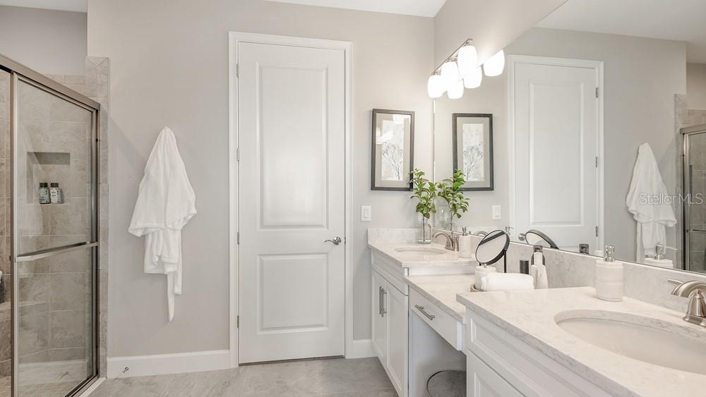 A modern bathroom features a double vanity with marble countertops, a glass shower, and white cabinetry — 7528 MOONBEAM AVENUE, SARASOTA, FL