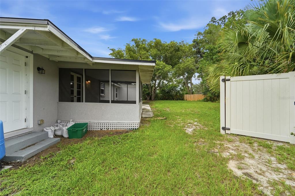 A view of a house exterior featuring a screened-in porch, a white fence, and lawn — 259 COLOMBA ROAD, DEBARY, FL