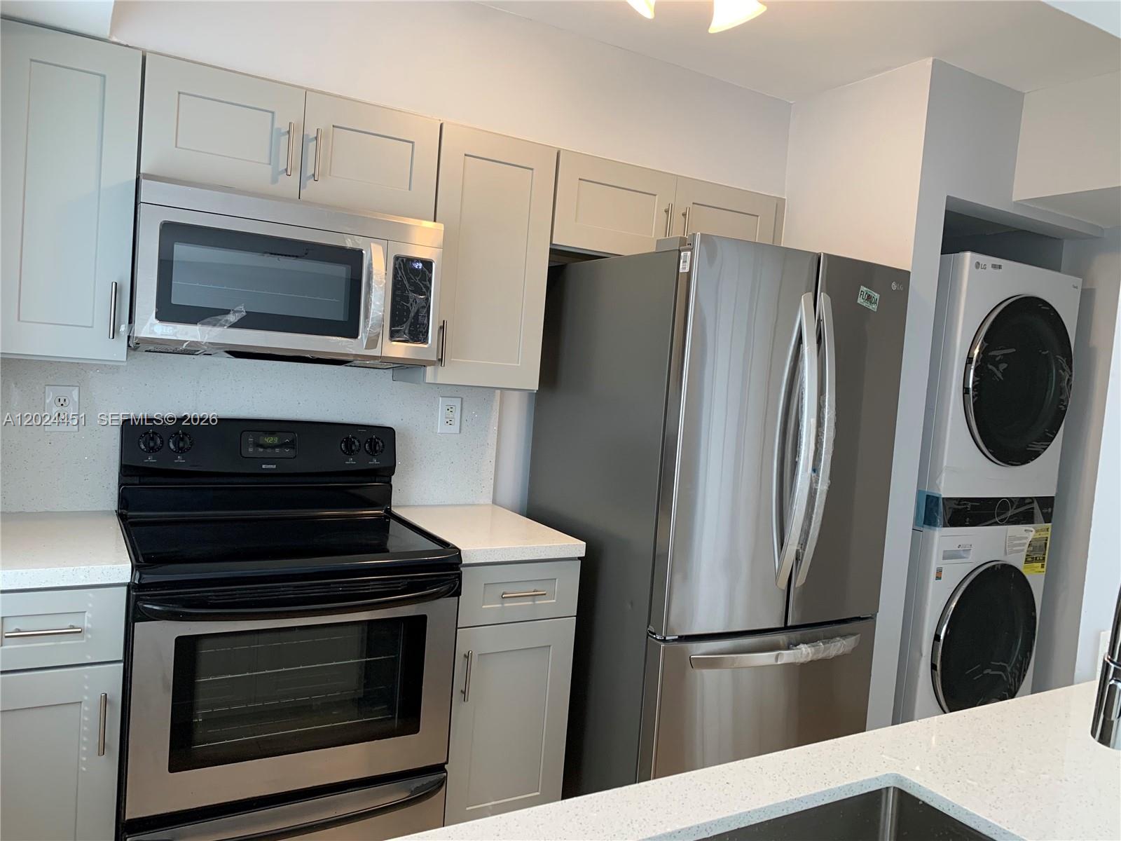 A kitchen features light gray cabinets, stainless steel appliances, and a stacked washer and dryer — 143 Riviera Cir # 143, Weston FL 33326, WESTON, FL