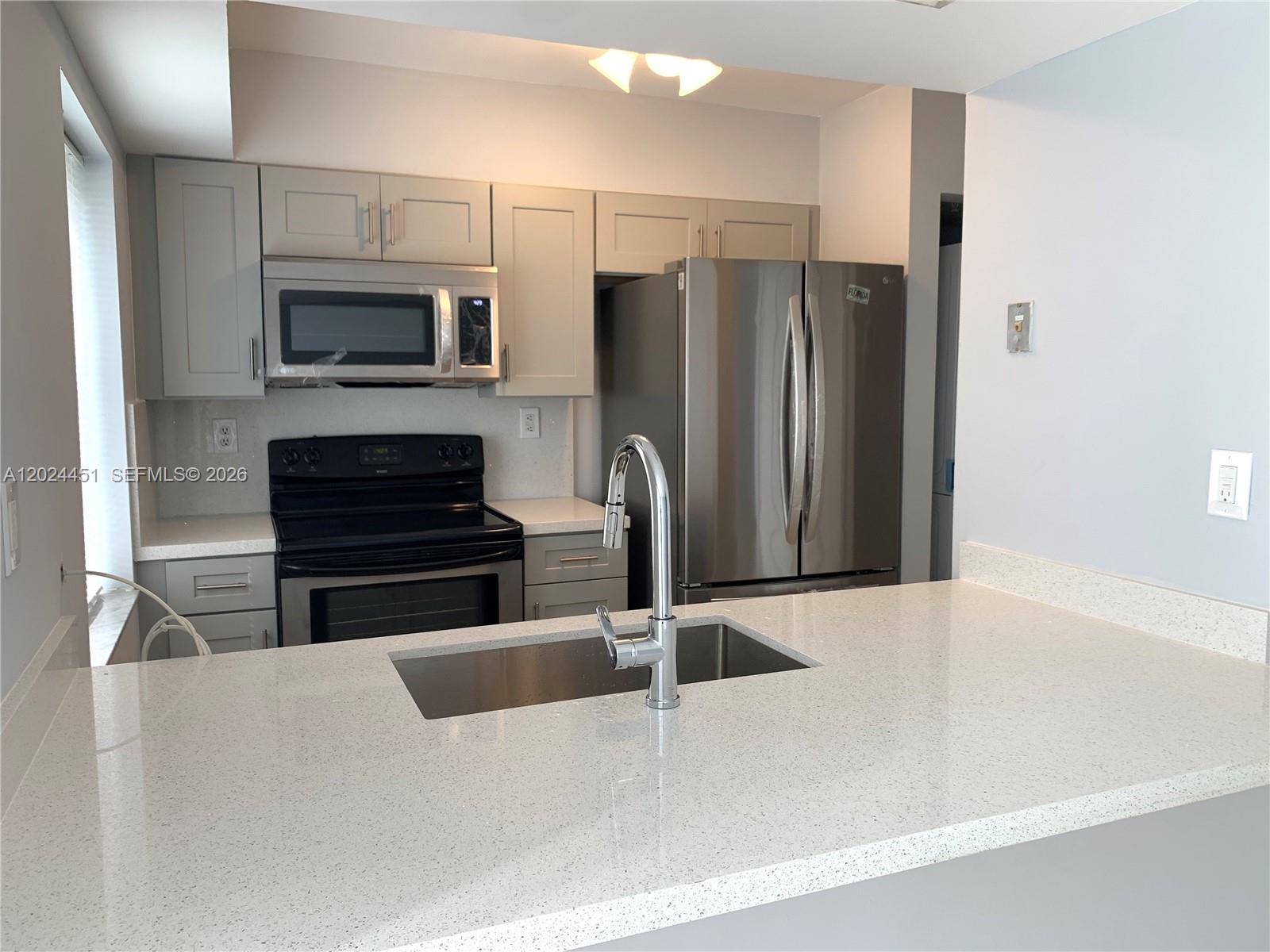 A kitchen features stainless steel appliances, light gray cabinetry, and a stacked washer-dryer unit — 143 Riviera Cir # 143, Weston FL 33326, WESTON, FL