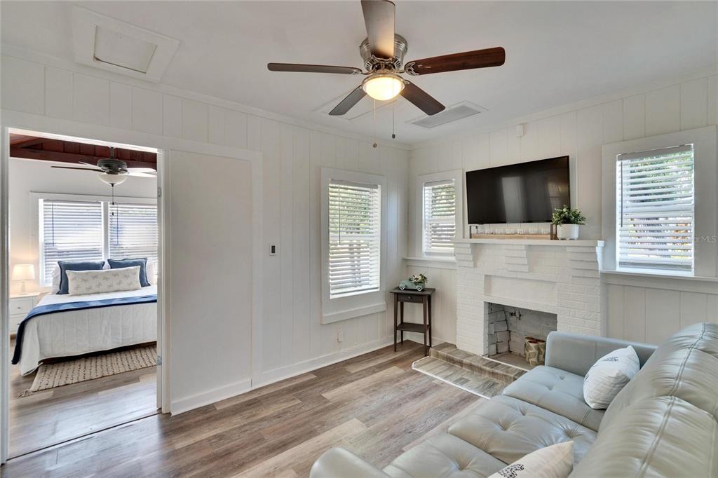 A living room with a white brick fireplace, wood-look flooring, and an adjacent bedroom — 1138 HOWARD STREET, CLEARWATER, FL