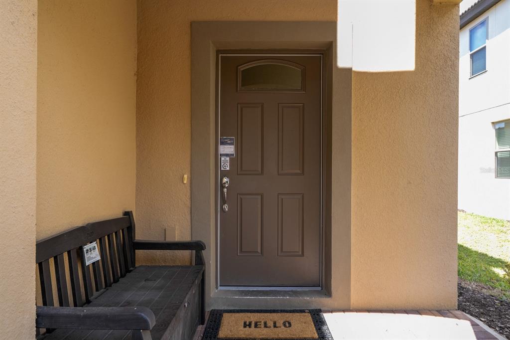 A brown front door with a small window sits under a covered entryway with a bench — 8877 BENGAL COURT, KISSIMMEE, FL