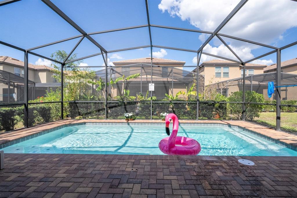 A screened-in patio features a rectangular swimming pool with a pink flamingo float — 8877 BENGAL COURT, KISSIMMEE, FL