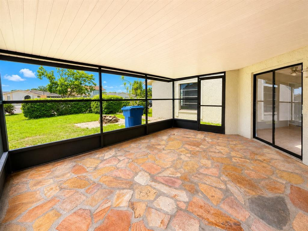 A screened-in patio features a flagstone floor and a view of a grassy backyard — 5104 SPRINGWATER COURT, TAMPA, FL