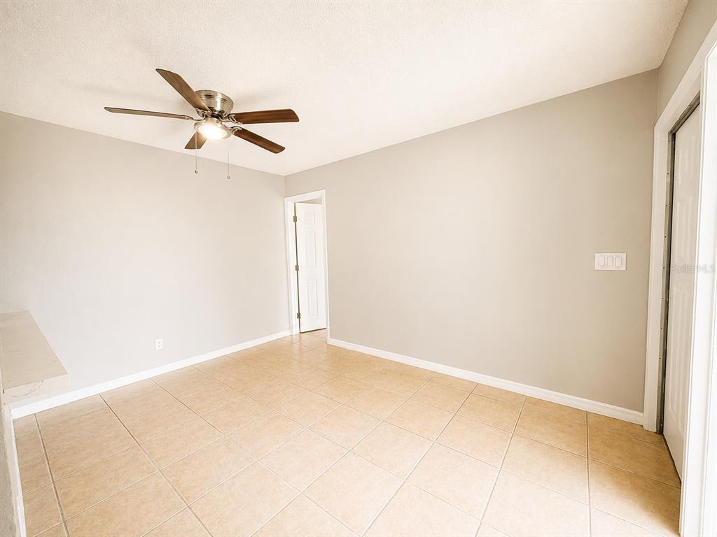An empty room with beige tile flooring, light gray walls, and a ceiling fan — 5104 SPRINGWATER COURT, TAMPA, FL
