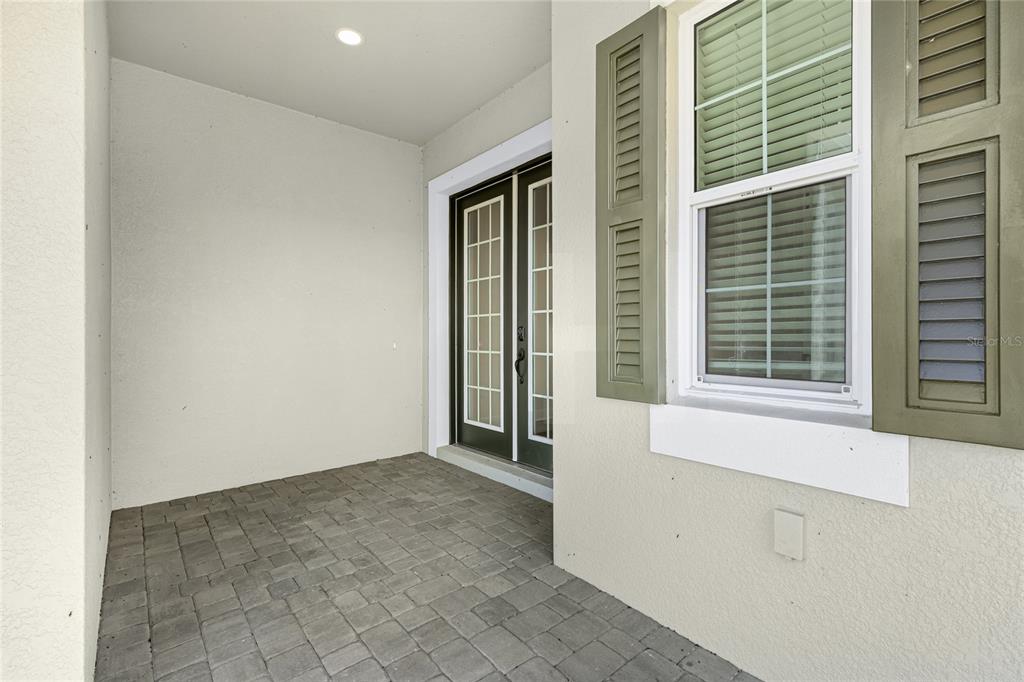 A covered patio features gray paver flooring, a double glass door, and a shuttered window — 2003 BAMBOO PALM COVE, BRADENTON, FL