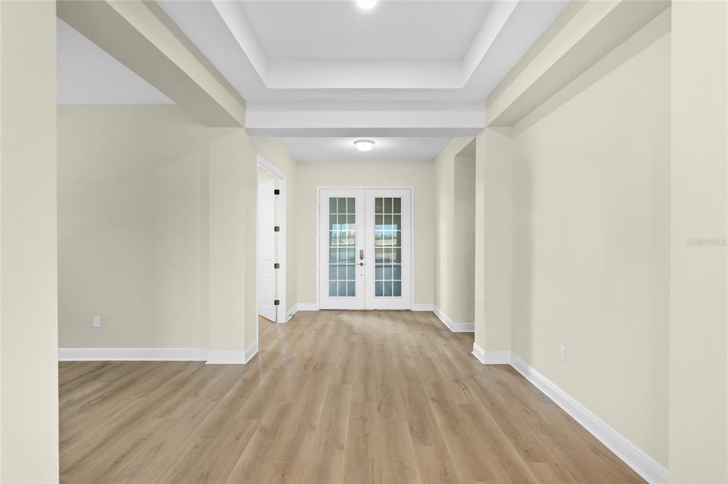 An empty room with light wood flooring, a tray ceiling, and white French doors — 2003 BAMBOO PALM COVE, BRADENTON, FL