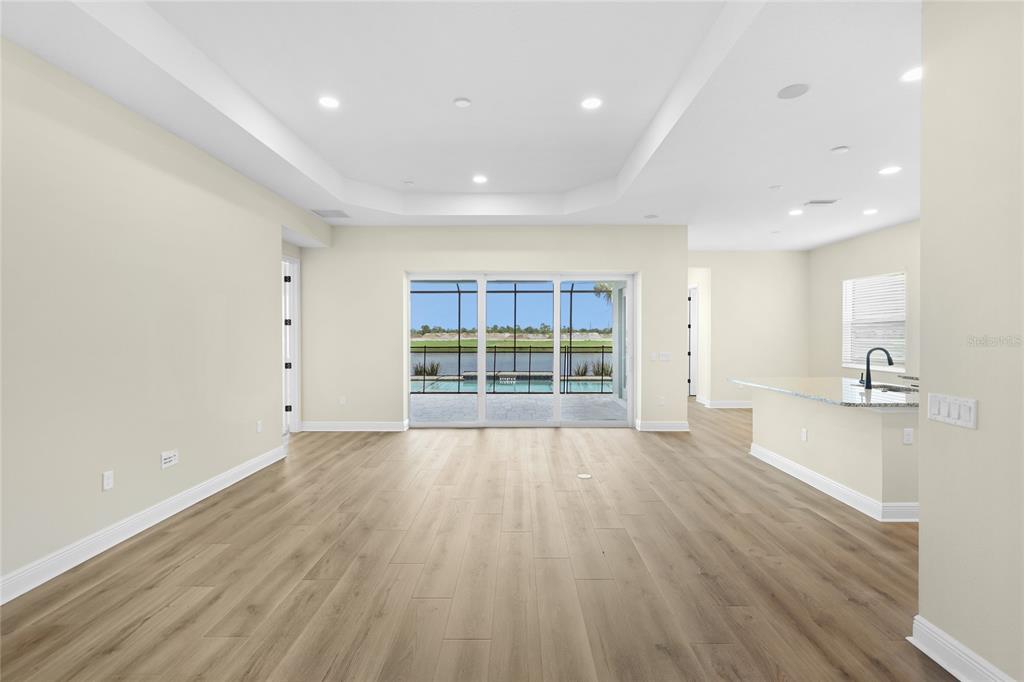 An open-concept living area with light wood-look flooring, recessed lighting, and sliding glass doors — 2003 BAMBOO PALM COVE, BRADENTON, FL