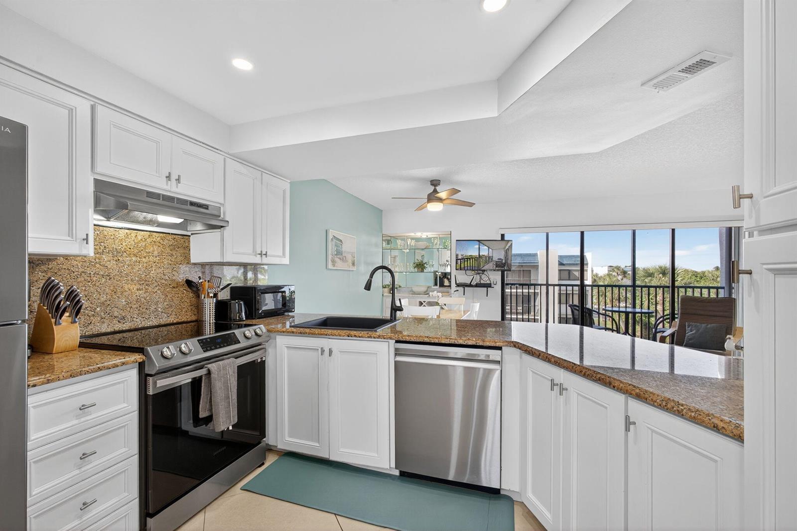A kitchen features white cabinets, granite countertops, stainless steel appliances, and a view of a balcony — 1605 S Us Highway 1 # A407, Jupiter FL 33477, JUPITER, FL
