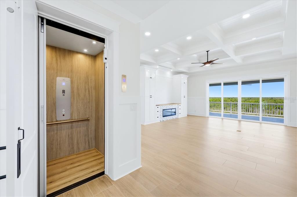 A residential elevator opens into a bright living room with light wood floors and coffered ceilings — 13220 ANGLERS WAY, PLACIDA, FL