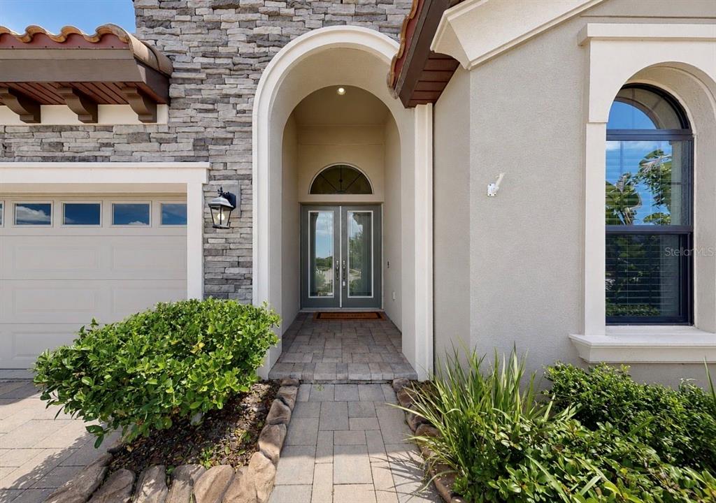 The exterior of a house features a stone facade, arched entryway, and double glass doors — 13712 OSPREY FERN LANE, RIVERVIEW, FL