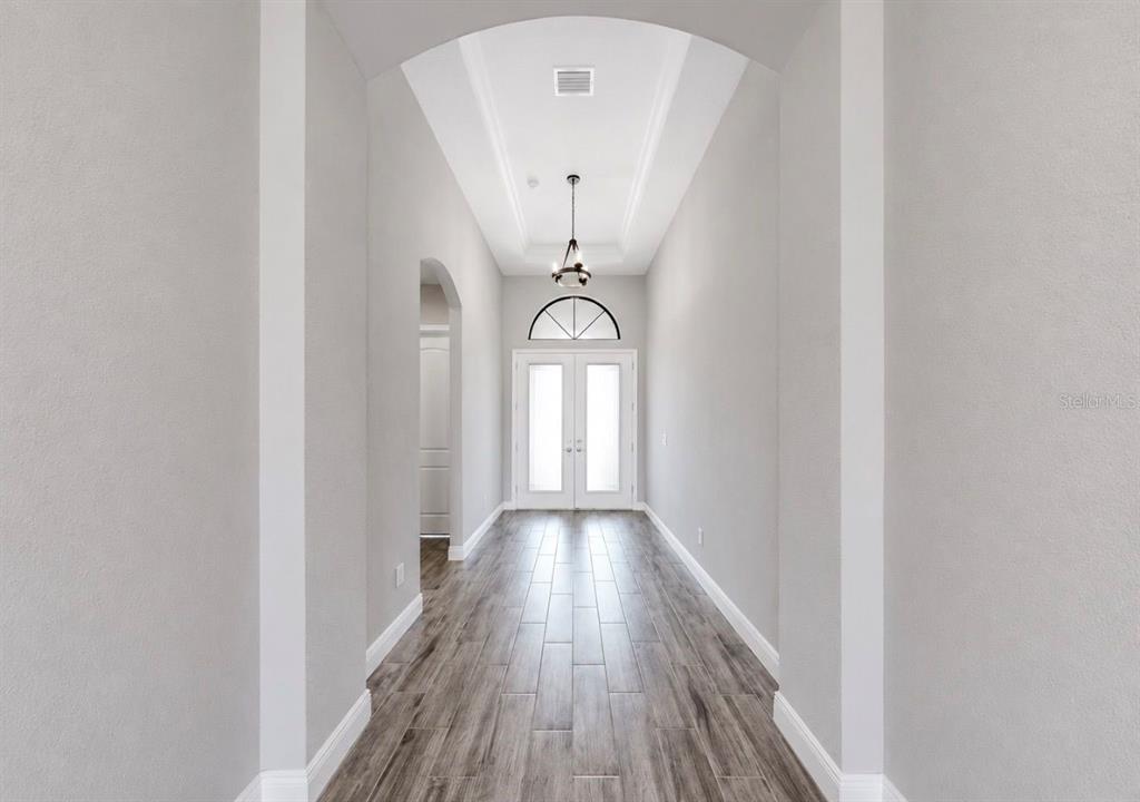 A bright entryway features a vaulted ceiling, a hanging light fixture, and wood-look tile flooring — 13712 OSPREY FERN LANE, RIVERVIEW, FL