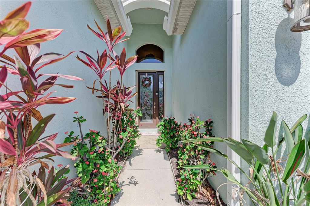 A concrete walkway leads to a front door flanked by potted plants and tropical foliage — 3728 SUMMERWIND CIRCLE, BRADENTON, FL