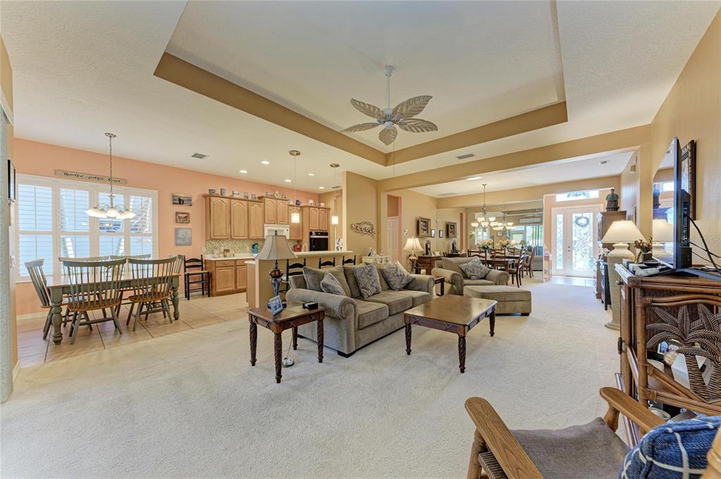 An open-concept living and dining area features a tray ceiling, beige carpeting, and wooden cabinetry — 3728 SUMMERWIND CIRCLE, BRADENTON, FL