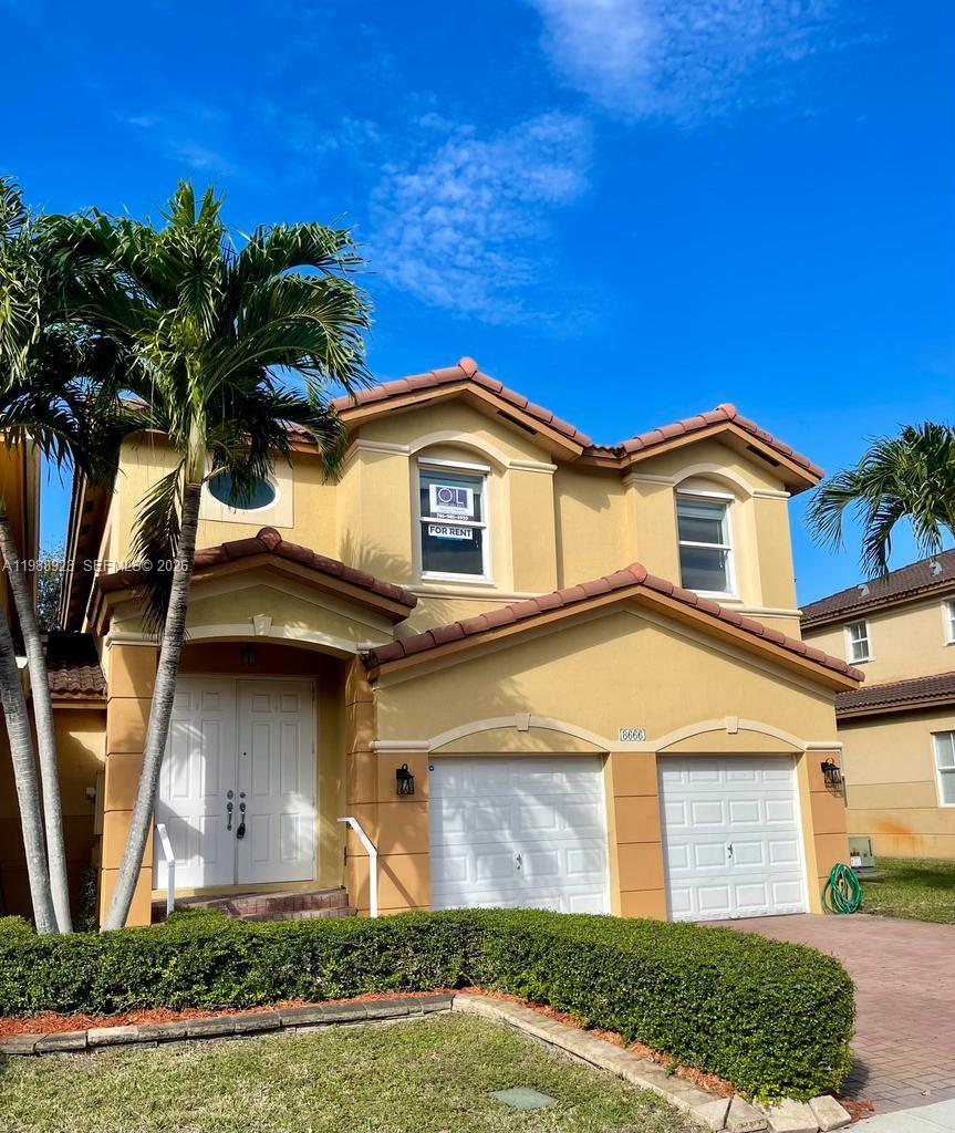 A two-story suburban house features a tan stucco exterior, a two-car garage, and palm trees — 8666 NW 109th Ct # 8666, Doral FL 33178, DORAL, FL